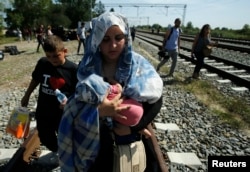 A migrant woman carries a baby as she walks on a railway track near Tovarnik, Croatia Sept. 17, 2015.