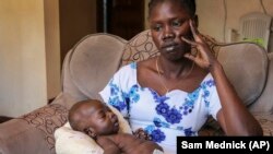 In this photo taken Thursday, Nov. 28, 2019, baby boy Ping Mayak Geer, who was born with six fingers on each hand, one stunted leg, a deformed foot and kidney swelling, lies on the lap of his mother Abui Mou Kueth in Nairobi, Kenya.