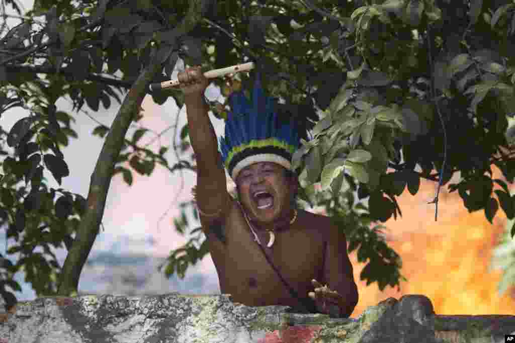 An indigenous man shouts to police, clutching a flute from inside the old Indian Museum where a fire burns behind in Rio de Janeiro. Police in riot gear invaded an old Indian museum complex and pulled out a few dozen indigenous people who for months resisted eviction from the building, which will be razed as part of World Cup preparations. 