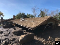 In this photo provided by Santa Barbara County Fire Department, mudflow, boulders, and debris from heavy rain runoff from early Tuesday reached the roof of a single story home in Montecito, Calif., on Jan. 10, 2018.