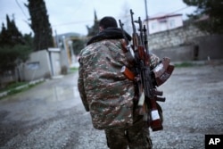 An ethnic Armenian fighter carries Kalashnikov machine guns to his comrade-in-arms at Martakert province in the separatist region of Nagorno-Karabakh, Azerbaijan, Monday, April 4, 2016.