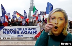 FILE - A person holds a mask of France's National Front (FN) defeated presidential candidate, Marine Le Pen, as people gather with French and European flags near the Eiffel Tower and a banner with the message, "France tells Hate: Never Again "