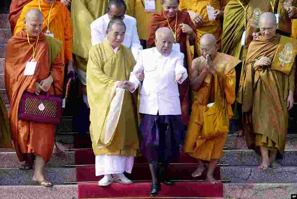 Then King Sihanouk, center, is helped down stairs at the Royal Palace in Phnom Penh, with help from Buddhist leaders attending the opening ceremonies of the World Buddhist Conference, December 5, 2002. 