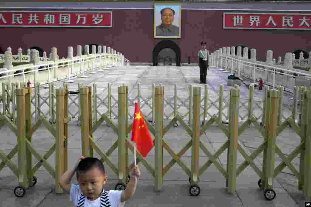 A child holds up a Chinese national flag as he poses for a photo in front of Tiananmen Gate in Beijing, June 4, 2014.
