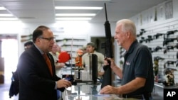 FILE - Sales associate Mike Conway, right, shows Paul Angulo a semiautomatic rifle at Bullseye Sport gun shop in Riverside, Calif., Dec. 9, 2015. Guns can be bought online without a background check.