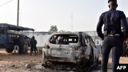 Un gendarme se tient devant l'épave d'une voiture brûlée, devant le centre des unités militaires d'élite du CCDO, Bouake, 10 janvier 2018.