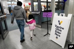 Seorang anak datang bersama orang tuanya untuk menerima vaksin Pfizer COVID-19 untuk anak-anak berusia 5 hingga 11 tahun di London Middle School di Wheeling, Ill., 17 November 2021. (Foto: AP)