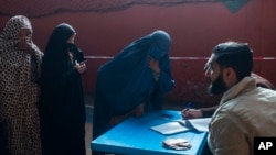 FILE - An Afghan woman registers her name to receive cash at a money distribution center, organized by the World Food Program in Kabul, Afghanistan, Nov. 17, 2021. The U.N. Security Council on Dec. 22, 2021, adopted a resolution aimed at facilitating aid to Afghanistan.