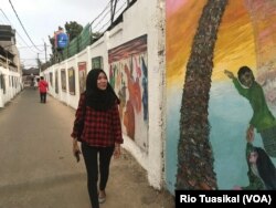 Mila Herliani, ibu rumah tangga yang tinggal di daerah itu, nampak menikmati karya yang dipajang Jitno Slamet di kawasan Cicendo, Bandung, Kamis, 23 Agustus 2018. (Foto: Rio Tuasikal/VOA)