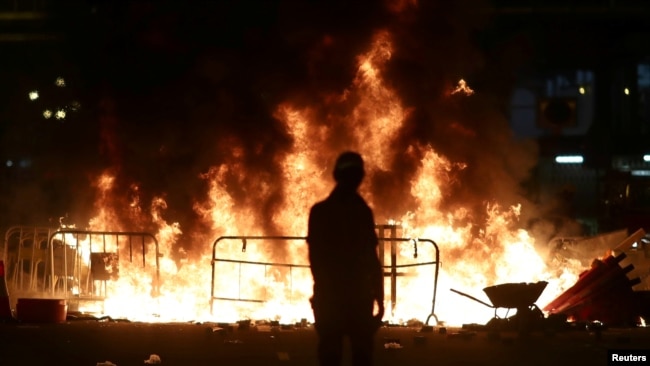2019年10月4日晚在香港特首宣布将实行禁蒙面法后一名抗议者站在黄大仙区街道上燃烧的一堆火旁。
