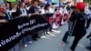 A disabled photographer, right, photographs protesters holding a banner that states: "Say No! Union, Association and NGO Laws" during a rally in front of the Senate building where senators voted on a draft of the Law on Associations and Nongovermental Organizations (LANGO), in Phnom Penh, Cambodia, Friday, July 24, 2015. 