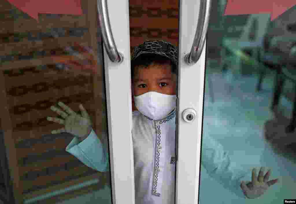 A Muslim boy wearing a protective face covering looks from his home near a closed mosque on the first day of the holy fasting month of Ramadan, amid the coronavirus disease (COVID-19) outbreak, in Bangkok, Thailand.