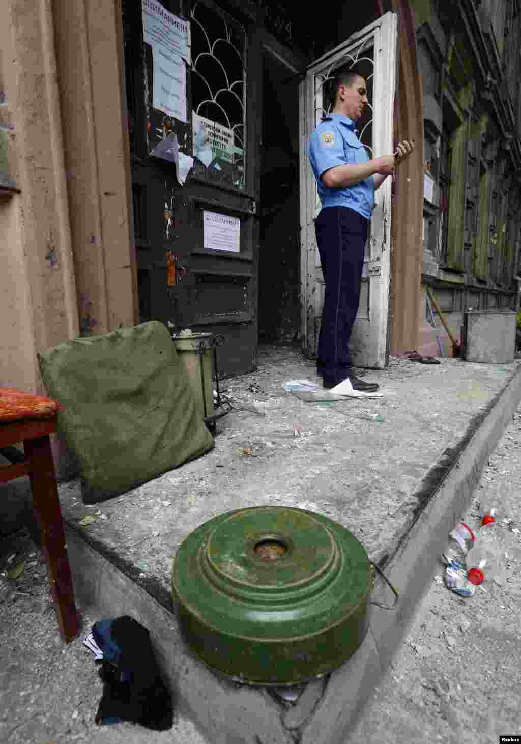 A policeman uses a mobile phone near an anti-tank mine at the site of fighting in the eastern Ukrainian port city of Mariupol, June 13, 2014. 