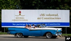 In this Oct. 2, 2018 photo, tourists take a joy ride in a vintage convertible car, past a billboard promoting constitutional reform