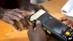 Une vieille femme nigériane valide sa carte de vote en utilisant un lecteur d'empreintes digitales, elle devra revenir plus tard dans la journée placer son bulletin de vote dans l'urne, dans la ville natale du candidat de l'opposition le général Muhammadu Buhari, en Daura, le Nigeria, samedi 28 mars 2015.