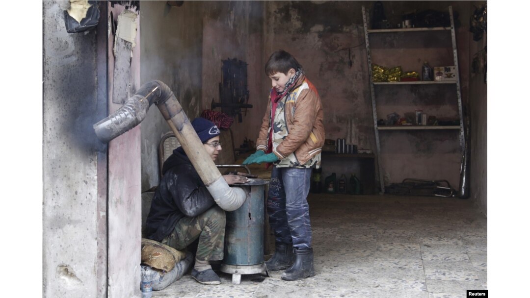 FILE - Boys warm themselves around a heater inside a shop during cold weather in the rebel-controlled area of Maaret al-Numan town in Idlib province, Syria, Jan 4, 2016.