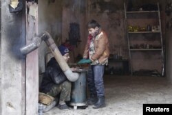 FILE - Boys warm themselves around a heater inside a shop during cold weather in the rebel-controlled area of Maaret al-Numan town in Idlib province, Syria, Jan 4, 2016.