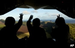 In this photo provided by the U.S. Air Force, Japan Air Self-Defense Force airmen wave at residents of the Commonwealth of the Northern Marianas island of Pagan as they drop a package to the islanders as part of Operation Christmas Drop.