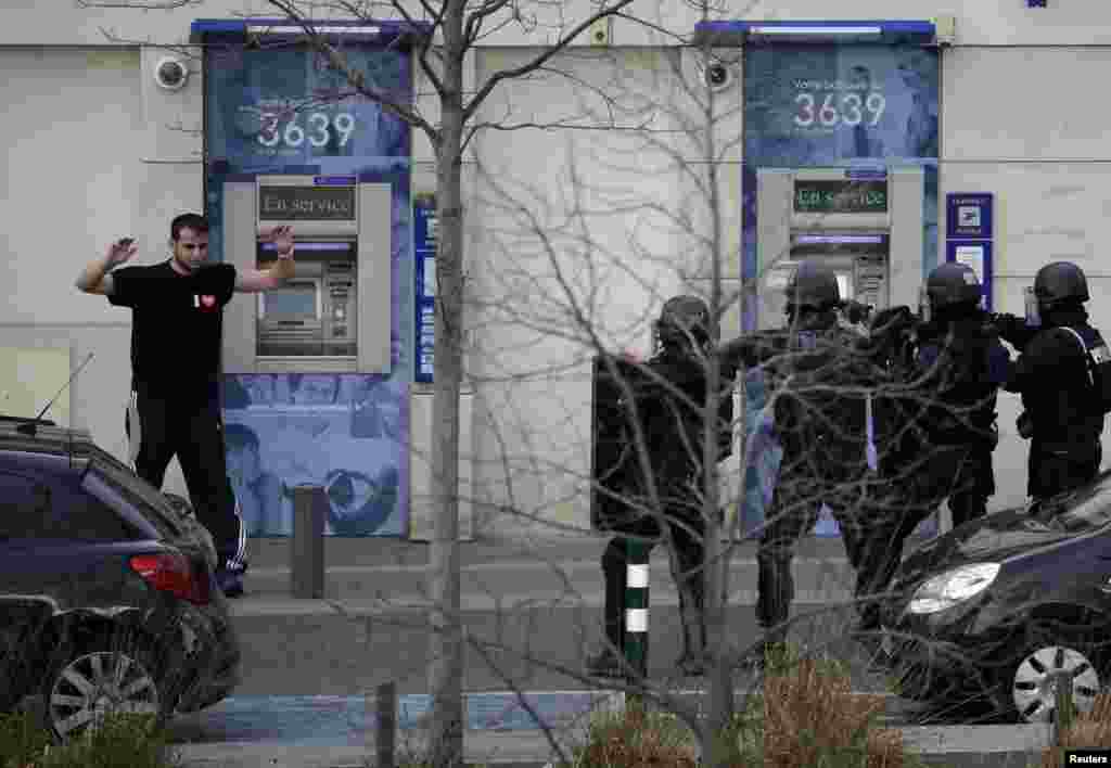 A suspect in a hostage taking situation raises his arms in the air as he is detained by members of special French RAID forces outside the post offices in Colombes outside Paris, Jan. 16, 2015.