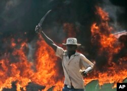 FILE - A supporter of the Orange Democratic Party holds up a machete in front of a burning barricade during riots in the Kibera slum in Nairobi, Kenya, Dec. 29, 2007.