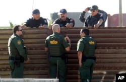 FILE - U.S. Customs and Border Protection’s acting deputy commissioner Ronald Vitiello, center foreground, and two other CBP agents, talk over the primary fence to their Mexican Federal Police counterparts in Tijuana, Mexico, Oct. 26, 2017, in San Diego.