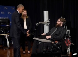 President Barack Obama shakes hands with Nathan Copeland, who demonstrates how he can control a robotic arm and feel when the robotic hand is touched. Dr. Jennifer Collinger, one of Copeland's doctors, watches.