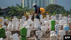 A worker pours water on newly planted flowers at a burial site for victims of the COVID-19 coronavirus at Keputih cemetery in Surabaya, East Java on July 15, 2020. (Photo by JUNI KRISWANTO / AFP)