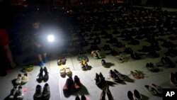 FILE - A child shines a light on hundreds of shoes at a memorial for those killed by Hurricane Maria, in front of the Puerto Rico Capitol in San Juan., June 1, 2018.