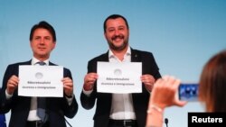 Italy's Prime Minister Giuseppe Conte and Interior Minister Matteo Salvini (R) hold up pieces of paper with the name of the new decree written on them as they are pictured during a news conference at Chigi Palace in Rome, Italy, Sept. 24, 2018. 