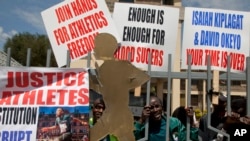 Athletes holds banners and look through the locked the gate at the Kenya Athletic offices in Nairobi, Kenya, Monday, Nov. 23, 2015. The International Association of Athletics Federations (IAAF) announced in November it has been investigating Kenya since March for allegations of covering up doping