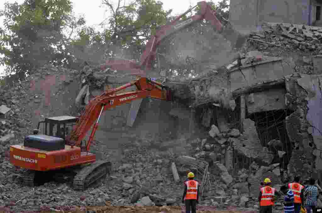 National Disaster Response Force workers look on as power shovels clear debris at the site of a collasped building in Canacona, India, Jan. 5, 2014. 