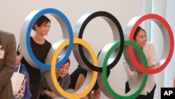 Orang-orang berfoto dengan tampilan Cincin Olimpiade di Bandara Internasional Haneda di Tokyo, Kamis, 8 Juli 2021. (Foto: AP/Koji Sasahara)