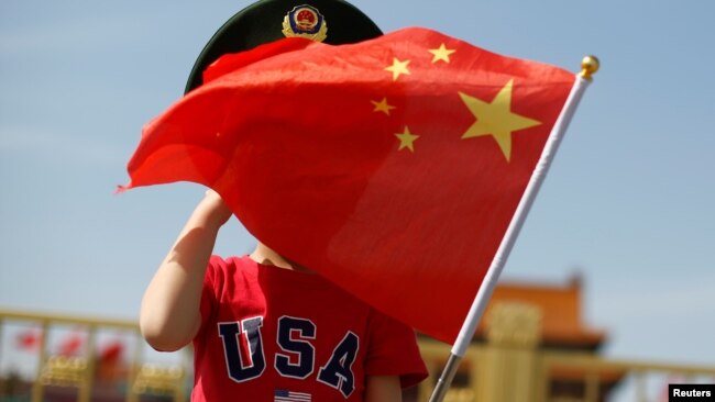 一名站在北京天安门广场的小男孩身穿美国T恤手拿中国国旗。（2019年5月7日）