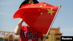 一名站在北京天安門廣場的小男孩身穿美國T恤手拿中國國旗。 （2019年5月7日）