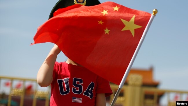 一名站在北京天安门广场的小男孩身穿美国T恤手拿中国国旗。（2019年5月7日）