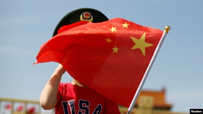 一名站在北京天安門廣場的小男孩身穿美國T恤手拿中國國旗。（2019年5月7日）