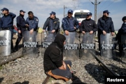 A migrant sits next to the riot police as other migrants block the railway track at the Greek-Macedonian border, near the village of Idomeni, Greece, March 3, 2016.