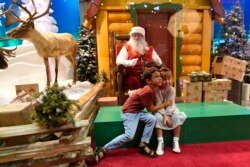 Theo and Sophy Morris, visiting from Hawaii with their family, pose for a photograph with Santa Claus, who is sitting behind a transparent barrier, at Bass Pro Shops, Friday, Nov. 20, 2020, in Miami.