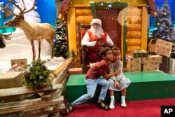 Theo and Sophy Morris, visiting from Hawaii with their family, pose for a photograph with Santa Claus, who is sitting behind a transparent barrier, at Bass Pro Shops, Friday, Nov. 20, 2020, in Miami.