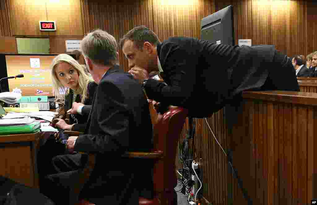Oscar Pistorius leans over to speak to his legal counsel from the dock in court on the third day of his trial at the high court in Pretoria, South Africa. Pistorius is charged with murder for the shooting death of his girlfriend, Reeva Steenkamp, on Valentine&#39;s Day in 2013.