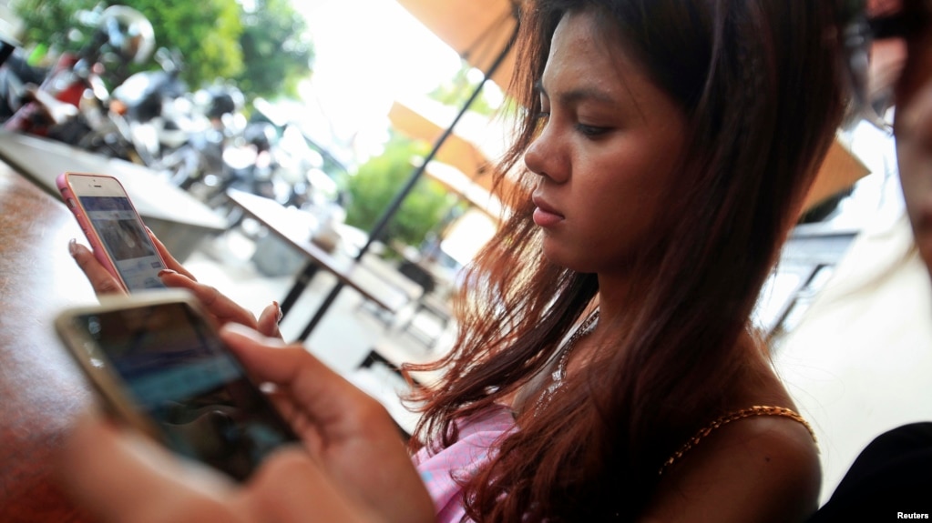 FILE - Online activist Thy Sovantha, 19, (L) and her friend use their mobile phones and social media in a cafe in Phnom Penh, Dec. 11, 2014. Security camera footage of the shooting of businessman Ung Meng Cheu went viral in Cambodia, illustrating the burgeoning power of social media in a youthful country where internet usage has soared in recent years. 