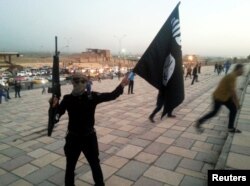 FILE - An Islamic State fighter hoists the terrorist group's flag and a weapon in the Iraqi city of Mosul, June 23, 2014.