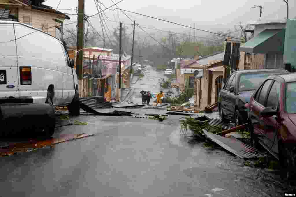 People walk on the street next to debris after the area was hit by Hurricane Maria in Guayama, Puerto Rico, Sept. 20, 2017.