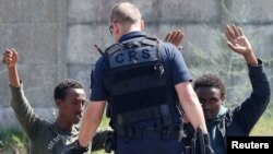 FILE - A French riot policeman approaches migrants who are on their knees as French authorities block their access to a food distribution point in Calais, France, June 1, 2017. Oxfam says French border police are mistreating migrant children.