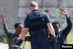 A French riot policeman approaches migrants who are on their knees as French authorities block their access to a food distribution point in Calais, France, June 1, 2017.