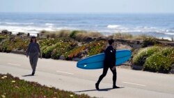 A surfer walks with his board across the car-free Great Highway toward the ocean in San Francisco, on April 28, 2021. (AP Photo/Eric Risberg)