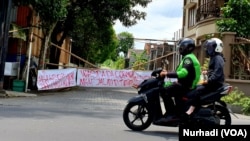 Ojek online melintas di gerbang kampung yang ditutup. Covid-19 berdampak besar pengemudi ojol. (Foto: VOA/Nurhadi)