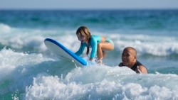 Eduardo Tanimoto teaches his five-year-old granddaughter Eloa how to surf at Maresias beach, in Sao Sebastiao, Brazil, Nov. 27, 2021.