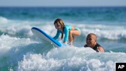Eduardo Tanimoto teaches his five-year-old granddaughter Eloa how to surf at Maresias beach, in Sao Sebastiao, Brazil, Nov. 27, 2021.