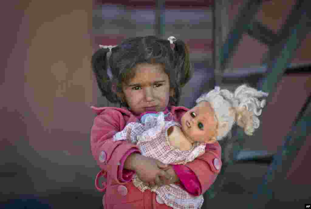 A girl holds a doll as refugees wait for the funeral convoy of a 19 year-old Syrian Kurdish fighter girl to pass by the camps in Suruc, on the Turkey-Syria border.